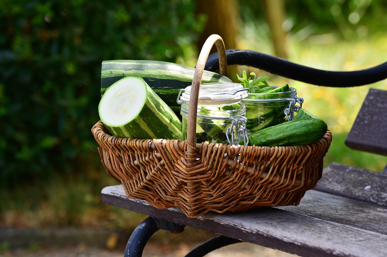 Weidenkorb mit Gurken, Zucchini und Einmachgläsern auf einer Parkbank im Freien.