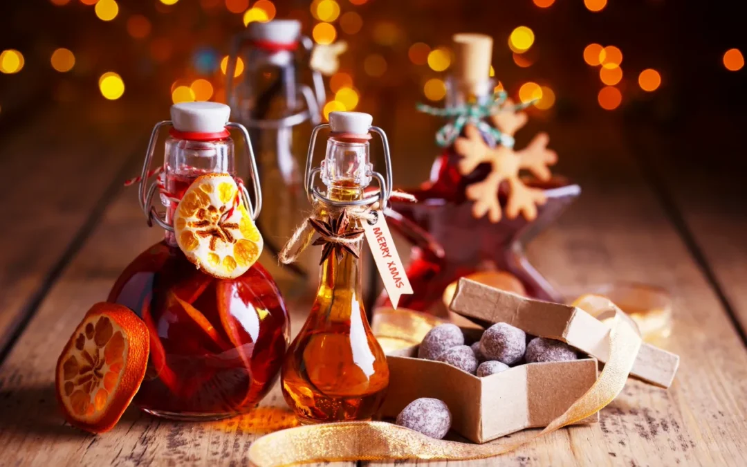 Weihnachtlich dekorierte Flaschen mit Gewürzen, getrockneten Orangen und eine Schachtel mit Pralinen auf Holztisch.