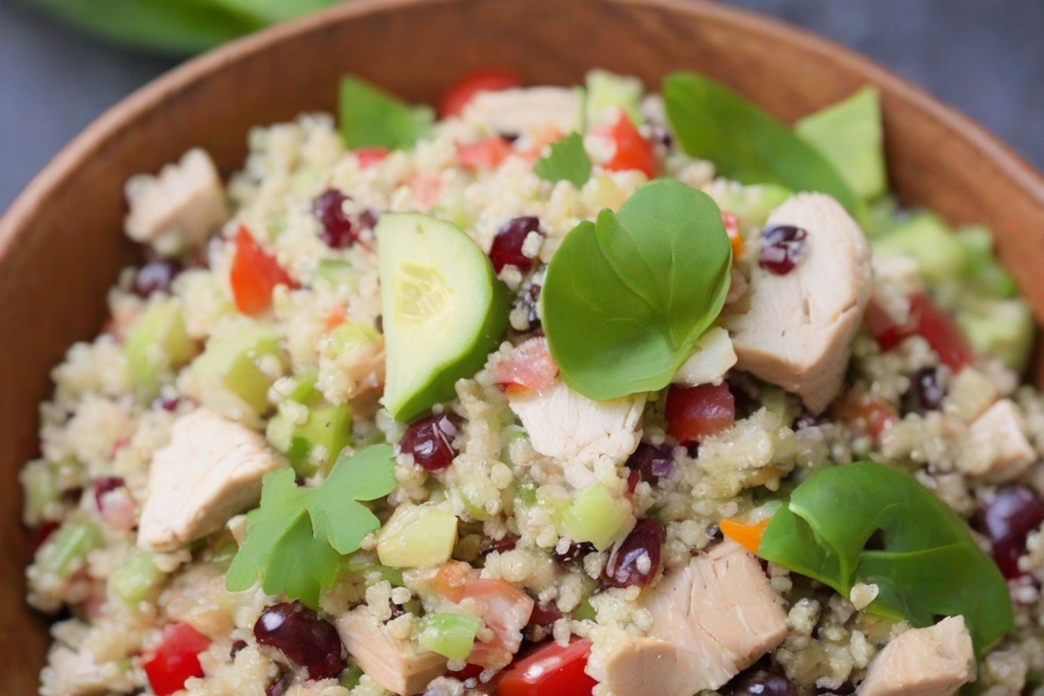 Bunter Couscous-Salat mit Hähnchen, Gurken, Paprika und frischen Kräutern in einer Holzschale.