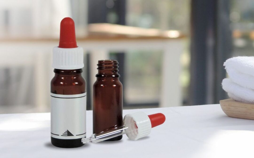 Zwei braune Tropfflaschen, eine mit weißem Etikett, Pipette und rote Spitze, auf einem Tisch vor unscharfem Hintergrund.