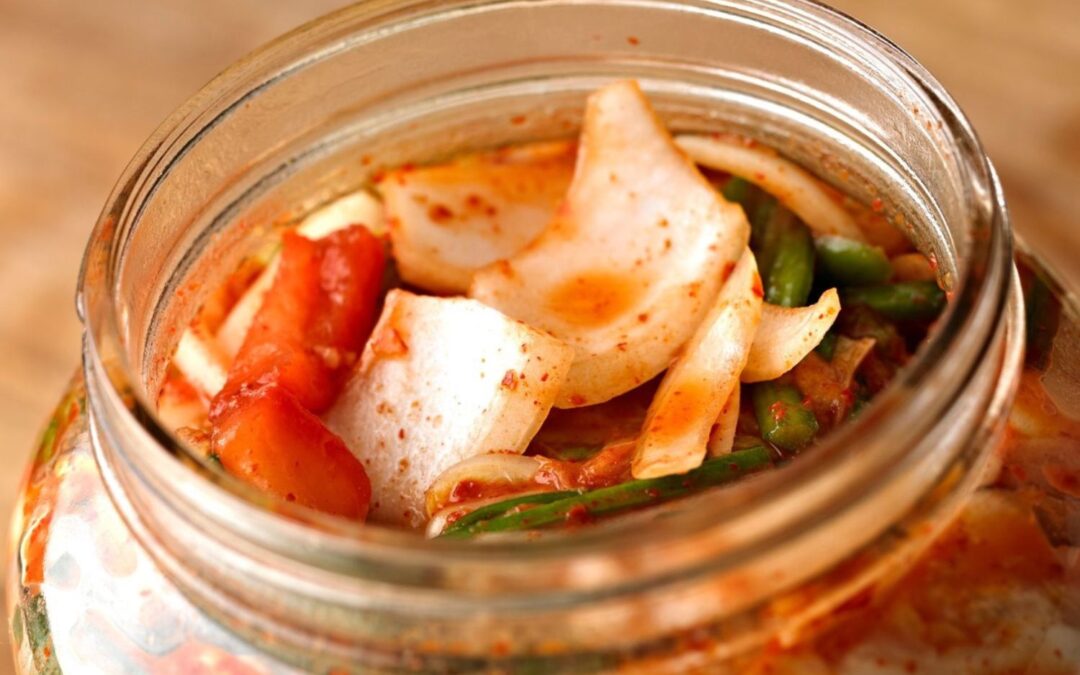 Offenes Glas mit Kimchi, bestehend aus fermentiertem Gemüse wie Kohl und Möhren, in roter Würzsauce.