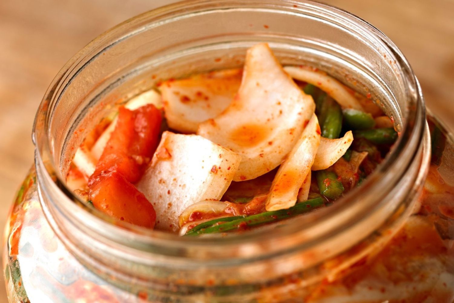 Offenes Glas mit Kimchi, bestehend aus fermentiertem Gemüse wie Kohl und Möhren, in roter Würzsauce.