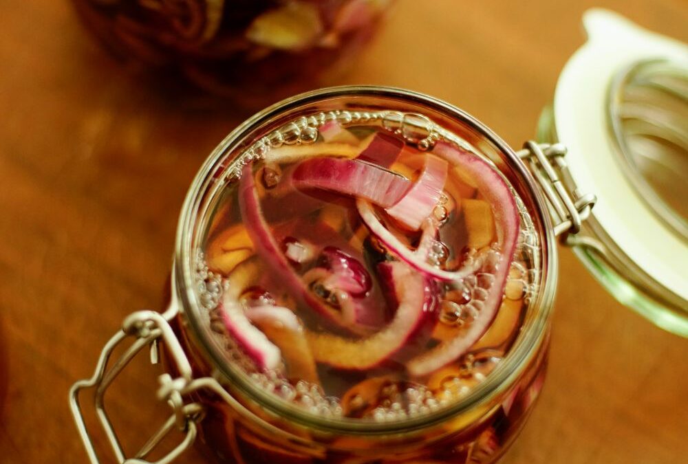 Eingelegte rote Zwiebeln in Glasbehältern auf einem Holztisch, Nahaufnahme.