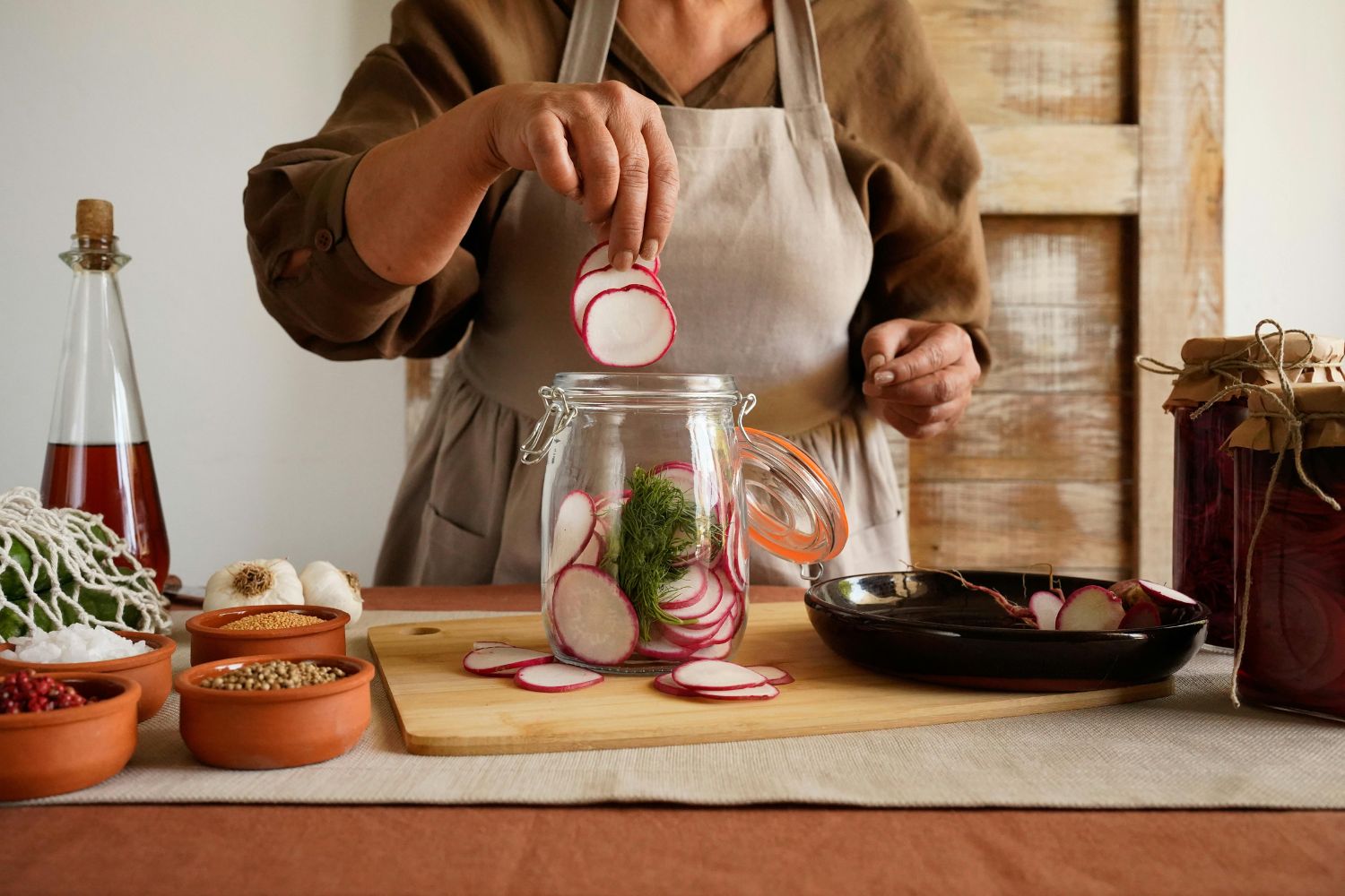 Radieschen fermentieren Person legt Radieschenscheiben in ein Glas auf einem Tisch mit Gewürzen und Knoblauch.