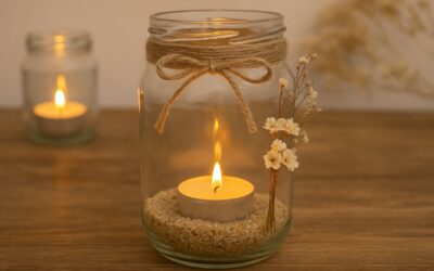Kerze in Glas mit Sand und Blumen, dekoriert mit Juteband, auf einem Holztisch; im Hintergrund weiteres Glas mit Kerze.