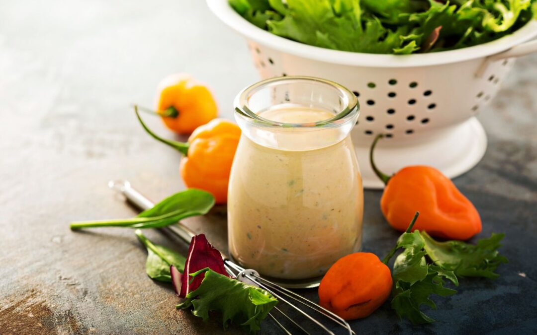 Ein Glas mit Dressing, umgeben von Habanero-Chilis und frischem Salat in einem weißen Sieb.