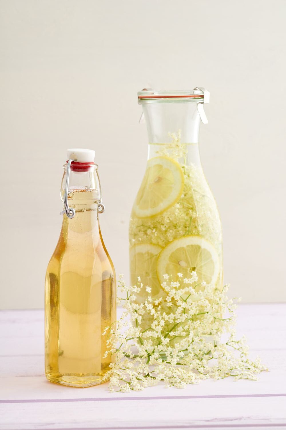 Holunderblütensirup Zwei Flaschen mit Holunderblütensirup, eine mit Zitronenscheiben. Weiße Holunderblüten liegen davor.