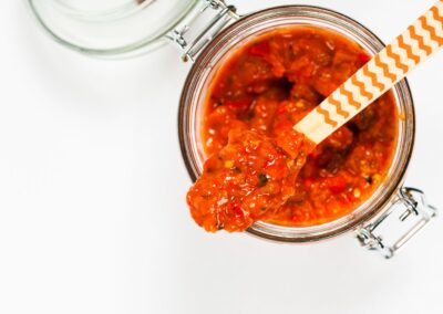 Geöffnetes Glas mit roter Sauce, Holzlöffel darin. Draufsicht, weiße Hintergrund.