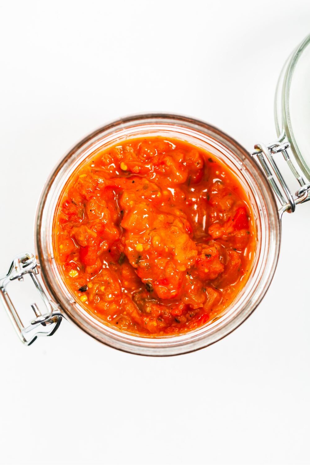 Aufstrich mit Paprika und frischen Kräutern Schraubglas mit roter, stückiger Soße, von oben fotografiert, auf weißem Hintergrund.