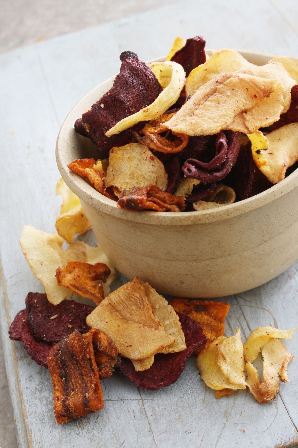 Schale mit bunten Gemüsechips auf Tisch, einige Chips sind herausgefallen.