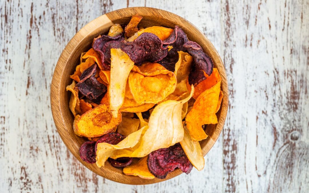 Holzschale mit bunten Gemüsechips auf rustikalem Holzuntergrund.