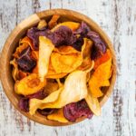 Holzschale mit bunten Gemüsechips auf rustikalem Holzuntergrund.