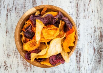 Holzschale mit bunten Gemüsechips auf rustikalem Holzuntergrund.