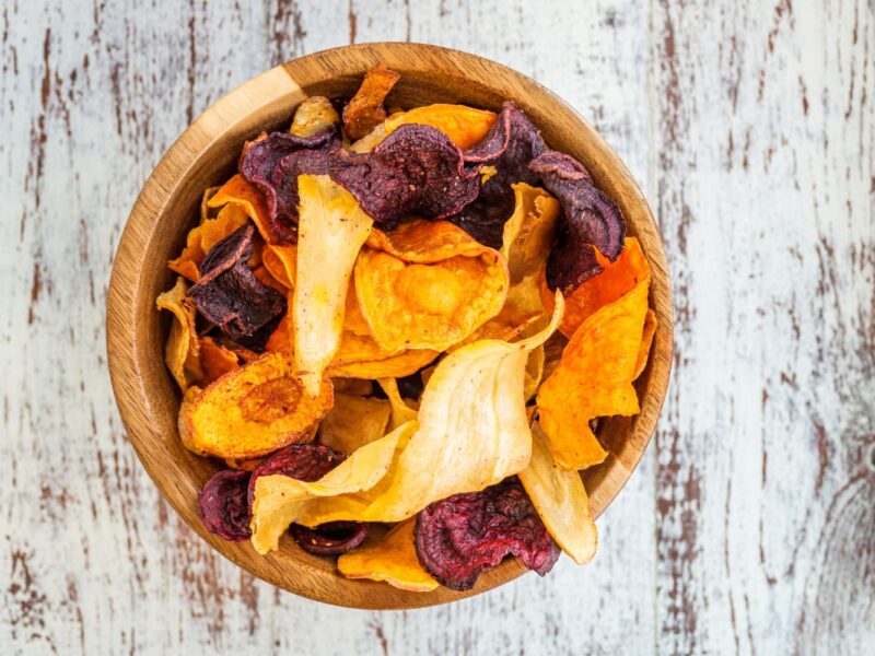 Holzschale mit bunten Gemüsechips auf rustikalem Holzuntergrund.