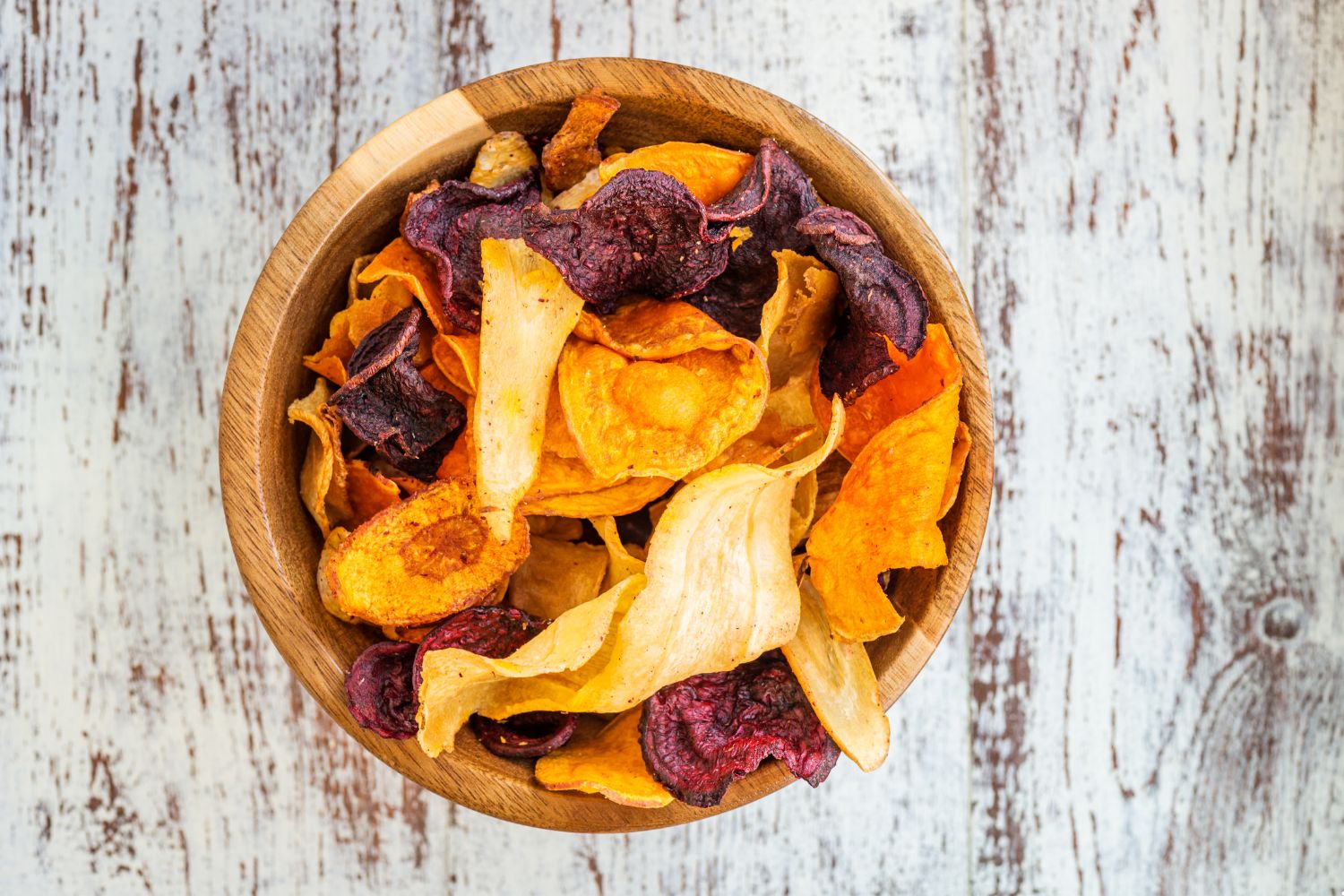 Holzschale mit bunten Gemüsechips auf rustikalem Holzuntergrund.