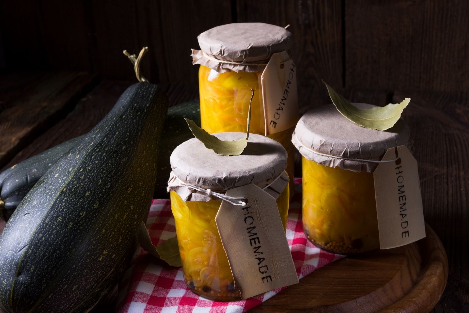 Selbstgemachte Marmelade im Einmachglas – Einkochen von Früchten leicht gemacht Zwei Hände halten ein Glas mit rotem Einkochgut über einem Tisch, auf dem weitere gefüllte Einmachgläser mit Metallklammern und Obst wie Erdbeeren und Kirschen stehen; im Hintergrund eine helle Küche mit grünen Pflanzen.